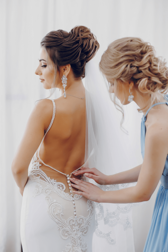 Подруга невесты помогает надеть свадебное платье